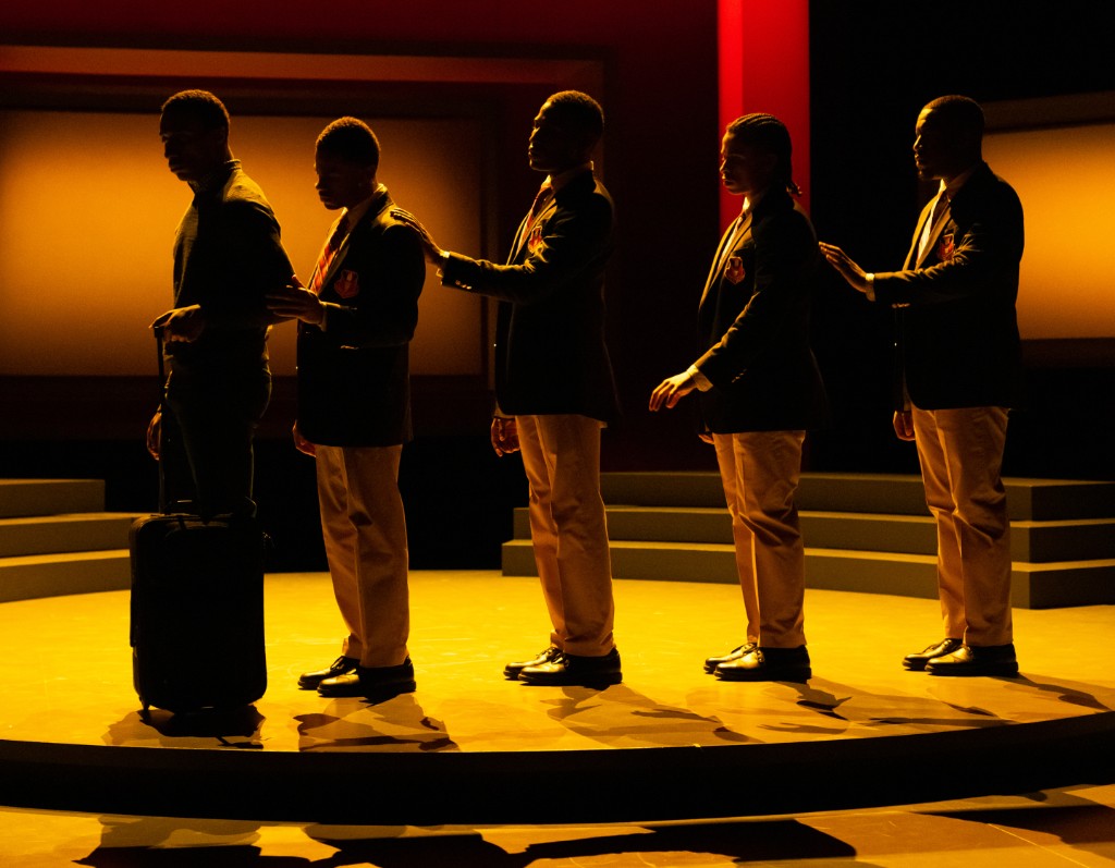 Five students in school blazers standing in a line on a lit stage