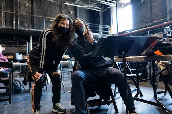 Diane Paulus leaning in beside Jeffrey L. Page at a music stand during a masked rehearsal